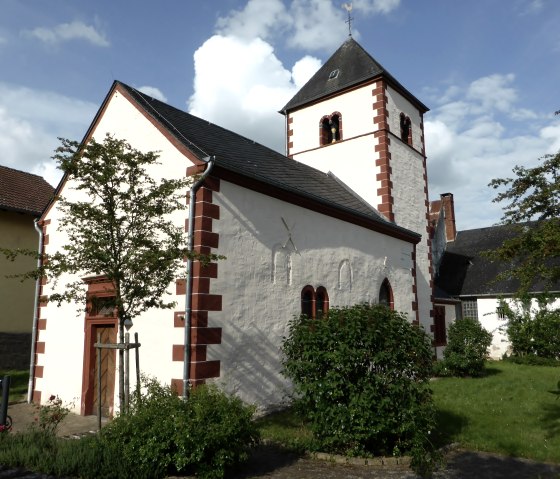 Small church with red brick pattern and tower, surrounded by trees and bushes under a blue sky., © Elke Wagner, Felsenland Südeifel Tourismus GmbH Small church with red brick pattern and tower, surrounded by trees and bushes under a blue sky., © Elke Wagner, Felsenland Südeifel Tourismus GmbH