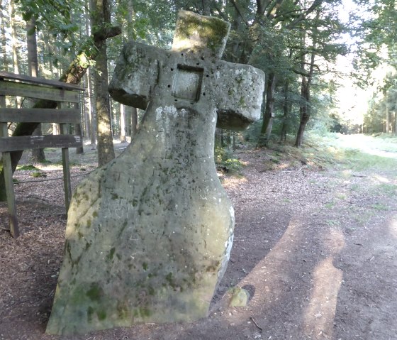 A stone cross, known as the Fraubille Cross, stands in the forest. It is surrounded by trees and a path leads through the clearing., © Elke Wagner, Felsenland Südeifel Tourismus GmbH A stone cross, known as the Fraubille Cross, stands in the forest. It is surrounded by trees and a path leads through the clearing., © Elke Wagner, Felsenland Südeifel Tourismus GmbH