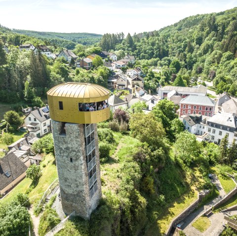 Une tour avec une plate-forme d'observation dorée surplombe un paysage verdoyant et une petite agglomération. Des forêts sont visibles à l'arrière-plan., © Eifel Tourismus GmbH, Dominik Ketz Une tour avec une plate-forme d'observation dorée surplombe un paysage verdoyant et une petite agglomération. Des forêts sont visibles à l'arrière-plan., © Eifel Tourismus GmbH, Dominik Ketz