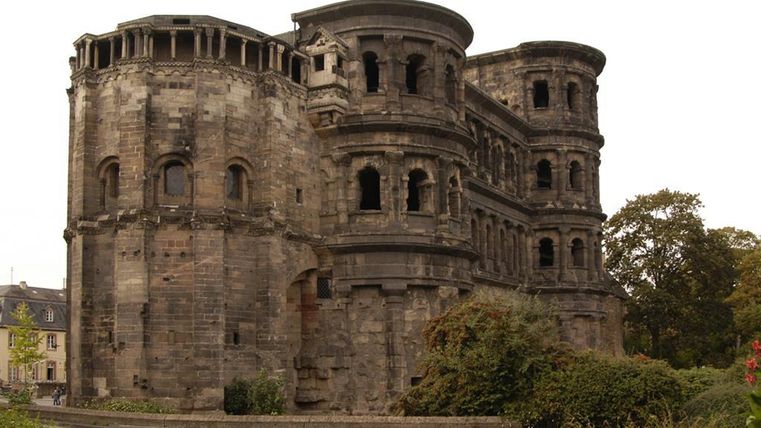 Eine alte römische Ruine mit vielen Fenstern und einer interessanten Architektur. Umgeben von Blumenbeeten und Bäumen.