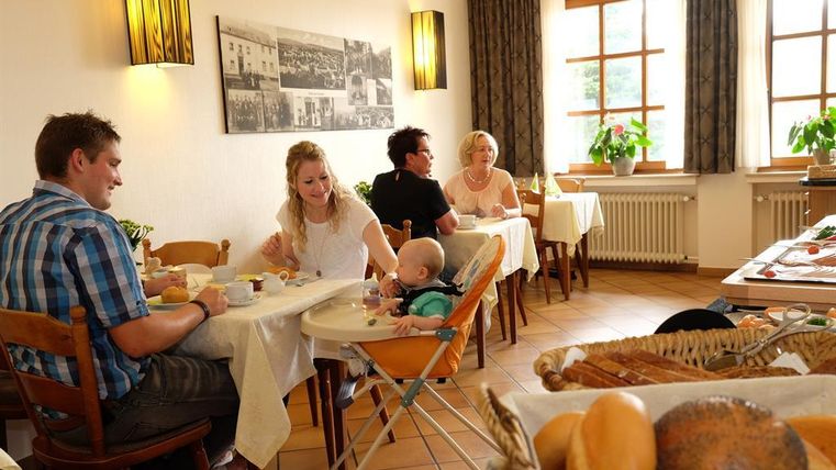 Ein gemütliches Restaurant mit einer Familie am Tisch. Auf dem Tisch sind verschiedene Frühstücksgerichte und frische Brötchen zu sehen.