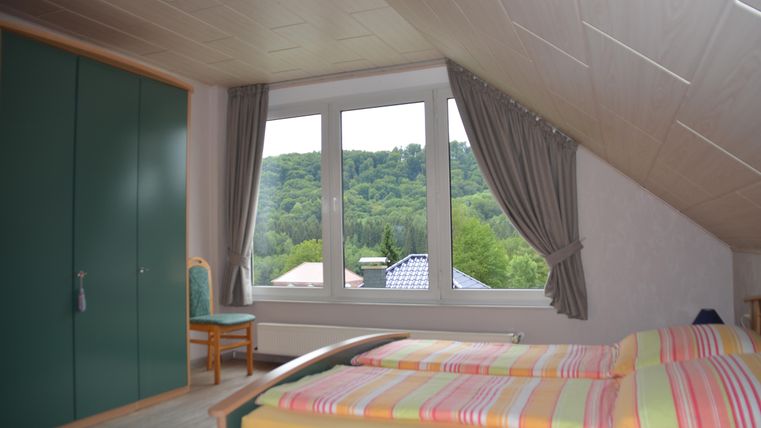 Ein helles Schlafzimmer mit einem Doppelbett und bunten Bettwäsche. Der Blick aus dem Fenster zeigt eine grüne Hügellandschaft.