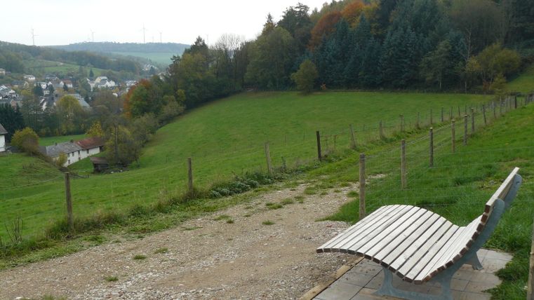 Eine Ruhebank mit Blick auf Mettendorf, umgeben von grünen Feldern und Bäumen.