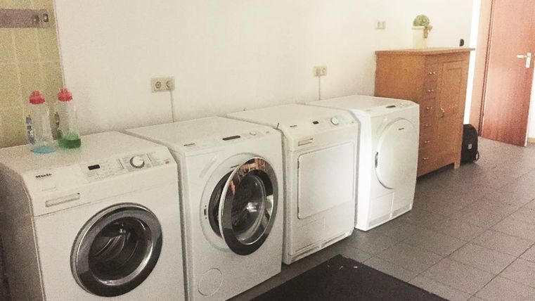 Ein Wäscheraum mit drei Waschmaschinen und einem Wäschetrockner. Rechts steht eine Kommode aus Holz.