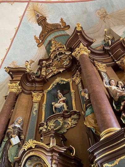 Ein prachtvoller Altarschrein mit künstlerischen Statuen und goldenen Verzierungen. Im Hintergrund sind malerische Deckenfresken zu sehen.