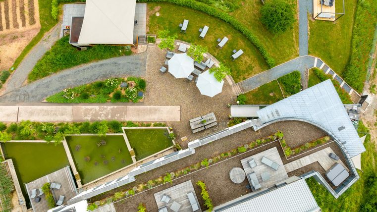 Eine moderne Gartenlandschaft mit Sitzbereichen und Wegen. Der Bereich umfasst Pflanzen, Wasserflächen und eine große Terrasse.