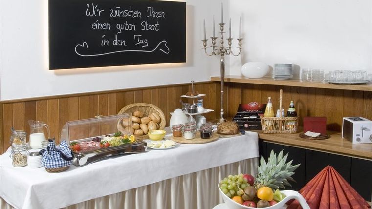 Ein Buffet mit einer Vielzahl von Frühstücksangeboten, darunter Brötchen, Obst und verschiedene Aufstriche. Im Hintergrund steht eine Tafel mit dem Wunsch für einen guten Start in den Tag.