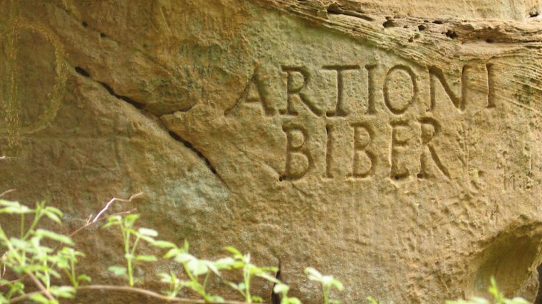 Eine Felswand mit eingravierten Worten. Unterhalb wachsen kleine Pflanzen.