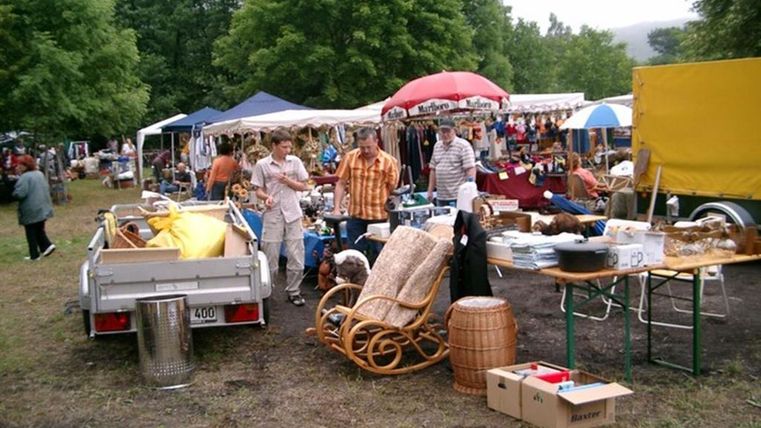 Ein Flohmarkt mit verschiedenen Ständen und Verkaufsständen. Menschen stöbern zwischen Möbeln und Haushaltswaren im Freien.