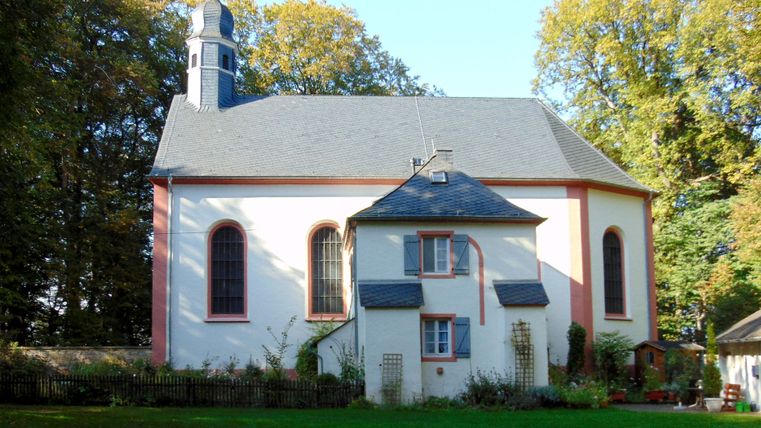 Schankweiler Klause, ein historisches Gebäude mit grauem Dach und weißen Wänden, umgeben von Bäumen.