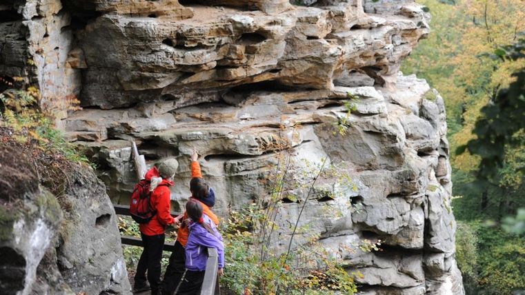Drei Personen auf einem Wanderweg in der Teufelsschlucht, die auf Felsformationen zeigen.