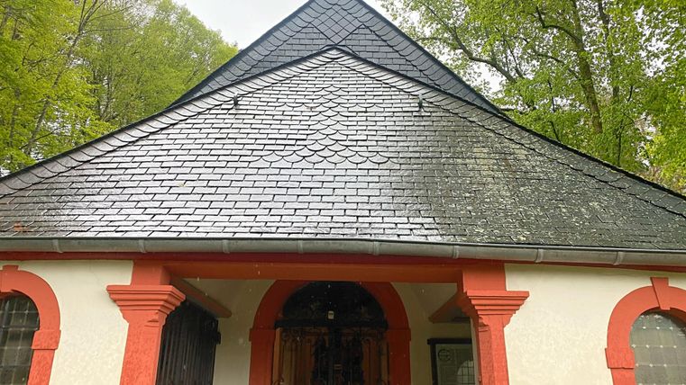 Ein historisches Gebäude mit einem schwarzen Dach und roten architektonischen Details. Umgeben von grüner Natur und Bäumen.