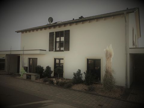 Een modern huis met witte muren en donkere luiken. Er zijn planten aan de voorkant en een schotelantenne op het dak.