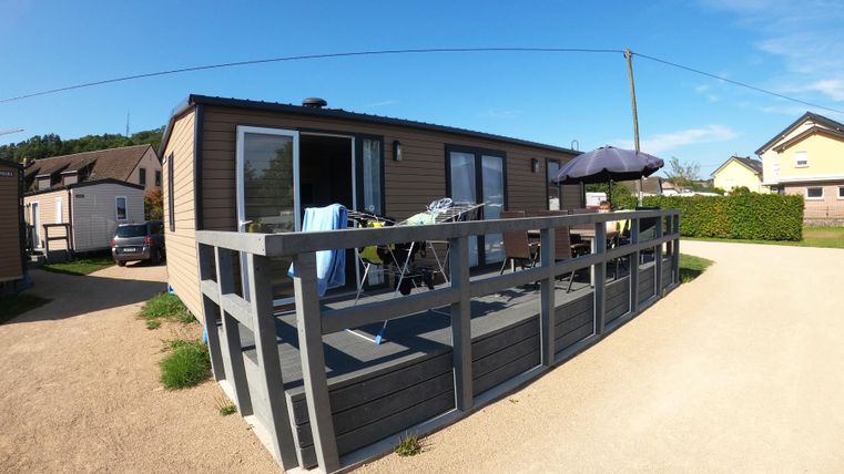 Ein modernes Ferienhaus mit einer Terrasse und Gartenmöbeln. Die Umgebung ist ruhig und grün, ideal für entspannende Tage.