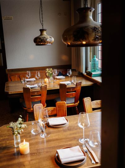 Ein einladendes Restaurant mit Holztafeln und Stühlen. Sanftes Licht von dekorativen Lampen schafft eine gemütliche Atmosphäre.