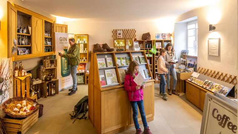 Ein gemütlicher Verkaufsraum mit Holzmöbeln und Regalen voller Produkte. Menschen schauen sich um und eine kleine Gruppe kauft ein.