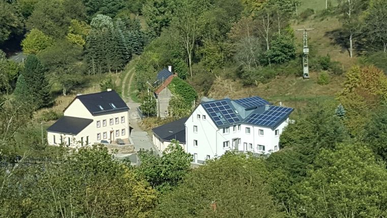 Deux maisons modernes dans un paysage verdoyant avec des arbres. La maison plus grande a des panneaux solaires sur le toit.