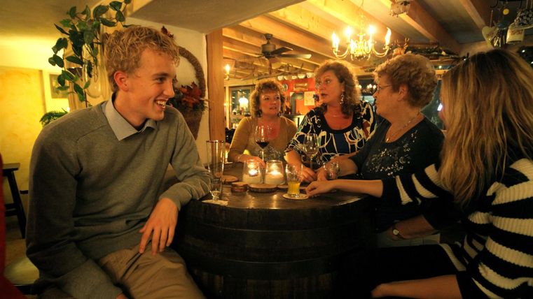 Eine gesellige Runde von fünf Personen in einem gemütlichen Restaurant. Sie sitzen um einen Tisch und unterhalten sich fröhlich.