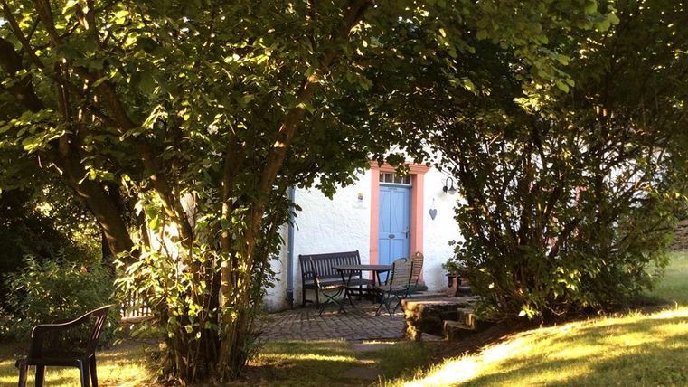 Ein schöner Garten mit einem gemütlichen Sitzbereich und viel Grün. Im Hintergrund sieht man ein Haus mit einer blauen Tür.