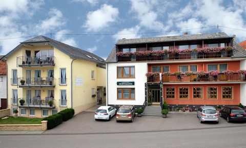 Un petit hôtel avec deux bâtiments et des balcons. Devant l'hôtel, il y a quelques voitures et le ciel est partiellement nuageux.