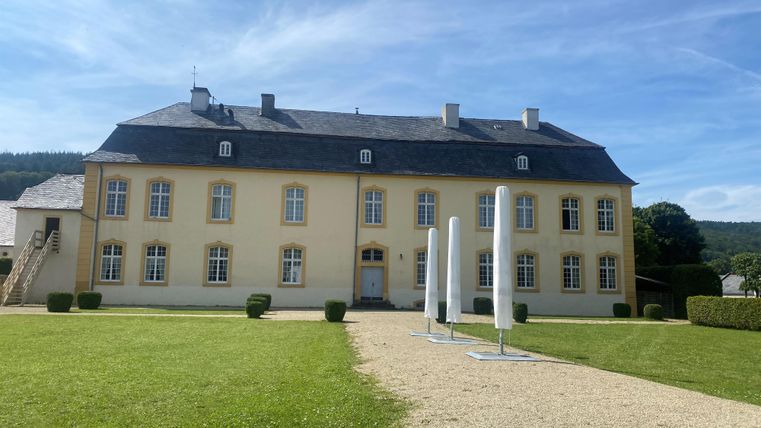 Ein schönes, gelbes Gebäude mit mehreren Fenstern und einem gepflegten Garten. Im Vordergrund stehen einige moderne Skulpturen.