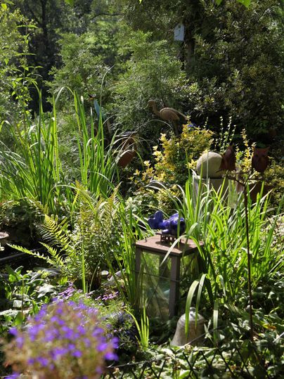 Ein üppiger Garten mit grünem Pflanzenwuchs und bunten Blüten. Eine Laterne steht auf dem Boden, umgeben von verschiedenen Pflanzen.