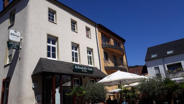 Ein charmantes Gebäude mit mehreren Fenstern und einem Eingang. Vor dem Haus stehen Sonnenschirme und Pflanzen.