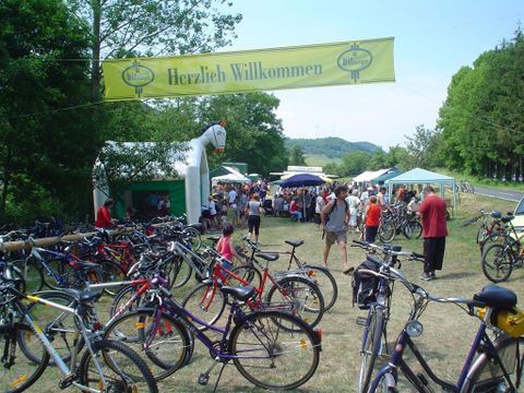 Ein belebtes Fest mit vielen Fahrrädern im Vordergrund. Im Hintergrund sind Menschen und Stände unter einem Willkommensbanner zu sehen.