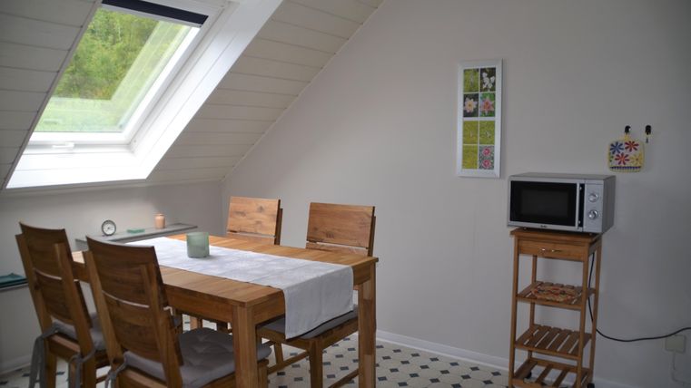 Ein heller Essbereich mit einem Holztisch und Stühlen. Ein Fenster lässt viel Licht herein, und ein Mikrowelle steht auf einem kleinen Tisch.