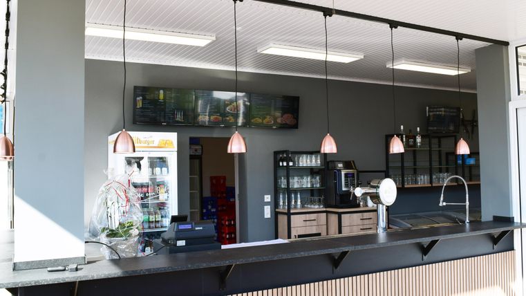 Ein moderner Kassenbereich mit hängenden Lampen und einem klaren, aufgeräumten Design. Im Hintergrund sind einige Geräte und Regale sichtbar.