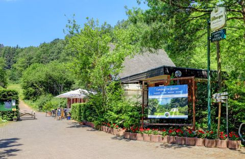 Ein gemütliches Restaurant inmitten der Natur mit grünen Bäumen und bunten Blumen. Der Weg führt zum Eingangsbereich, wo Tische im Freien stehen.