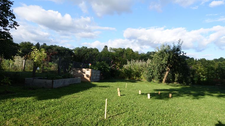 Un beau jardin avec de l'herbe verte et des arbres. En arrière-plan, on peut voir des plates-bandes de fleurs et un ciel bleu.