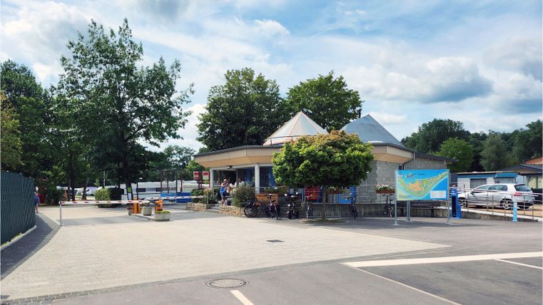 Ein Rundbau mit einem großen Schirmdach steht in einer ruhigen Umgebung. Grünflächen und Bäume umgeben den Bereich, der zum Entspannen einlädt.