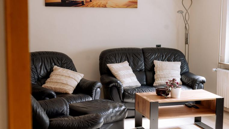 Een gezellige woonkamer met zwarte leren banken en een houten tafel. Aan de muur hangt een modern schilderij en er staat een vloerlamp.