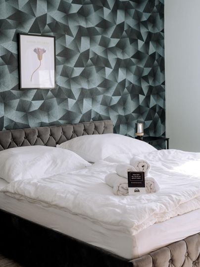 Een stijlvolle slaapkamer met een gestoffeerd bed en elegante beddengoed. De geometrische wandbekleding en het kunstwerk geven de ruimte een moderne uitstraling.