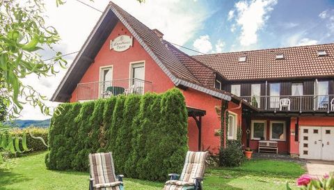 Une maison rouge avec un jardin verdoyant et des chaises longues confortables. Le ciel est clair et il y a une atmosphère calme.