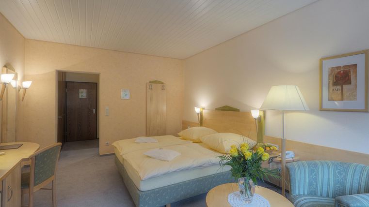 Ein gemütliches Hotelzimmer mit zwei Betten, einem Tisch und einer Sitzgelegenheit. Auf dem Tisch steht eine Vase mit frischen Blumen.