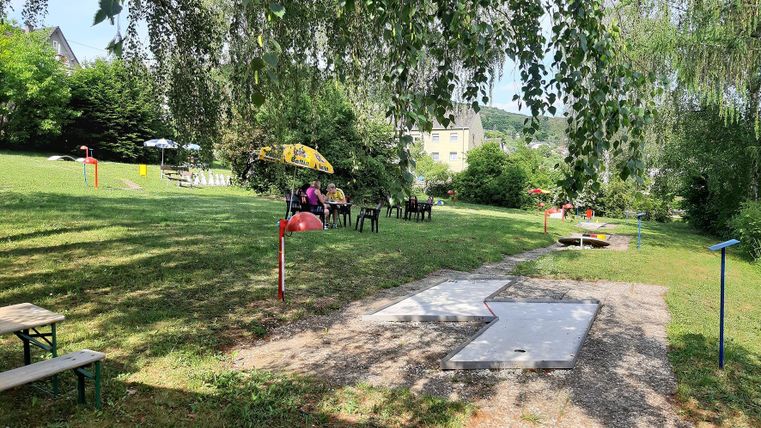 Ein ruhiger Garten mit Sitzgelegenheiten und einem wunderschönen, grünen Rasen. Es gibt einige Schirme und Spielbereiche für Aktivitäten.