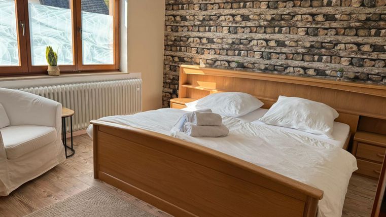 Een gezellige slaapkamer met een tweepersoonsbed en frisse witte dekbedden. De kamer heeft grote ramen en een mooie stenen muur.