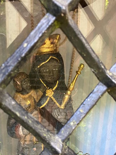 Eine Statue von einer schützenden Heiligen mit einem Kind in den Armen. Die Figur trägt eine Krone und hält einen Zepter, hinter einem Gitterfenster.