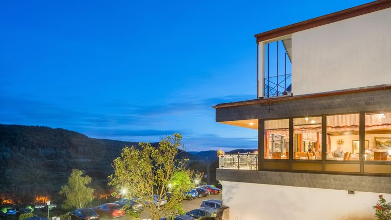 Das Waldhotel Sonnenberg am Abend mit großen Fenstern. Im Hintergrund ist eine ruhige Landschaft und parkende Autos zu sehen.
