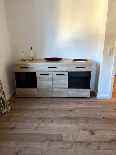 Ein moderner Sideboard aus Holz mit schwarzen Elementen. Darauf steht eine dekorative Schale und zwei kleine Figuren.