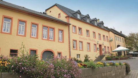 Un bâtiment historique avec une façade jaune et des accents rouges. Devant le bâtiment, des fleurs colorées fleurissent et il y a une terrasse avec des tables.