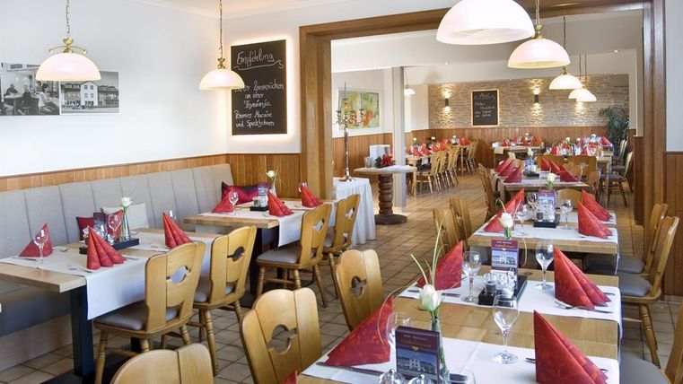 Ein gemütliches Restaurant mit Holzmöbeln und schön gedeckten Tischen. Rote Stoffservietten und eine einladende Atmosphäre schaffen ein angenehmes Ambiente.