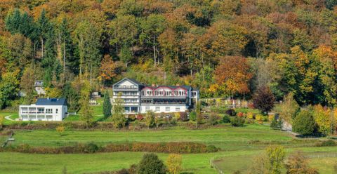 Ein malerisches Hotel umgeben von bunten Herbstbäumen. Die grüne Wiesenlandschaft bietet eine ruhige und idyllische Atmosphäre.