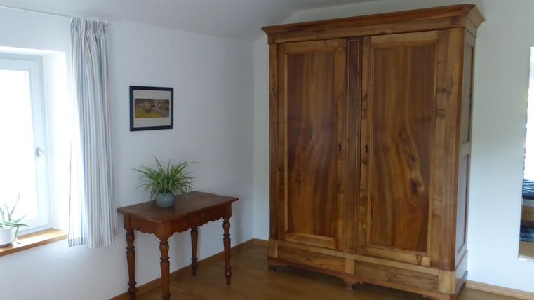 Ein gemütlicher Raum mit einem großen Holzschrank und einem kleinen Tisch. Die Fenster lassen viel natürliches Licht herein.