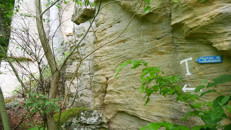 Felswand mit Wegweiser zum Teufelsloch im Wald.