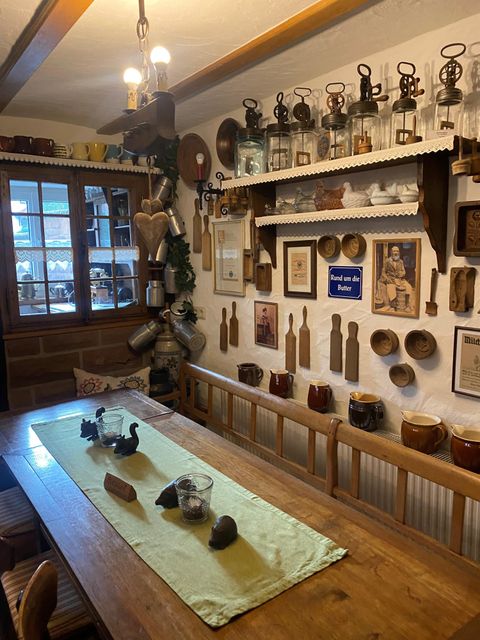 Ein gemütlicher Raum mit einem großen Holztisch und nostalgischer Dekoration an den Wänden. Alte Lampen und Küchenutensilien sind dekorativ angeordnet.