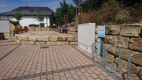 Eine gepflasterte Fläche mit einer Steinstufenbank und Fahrradständern. Im Hintergrund ist ein Gebäude und einige Pflanzen zu sehen.