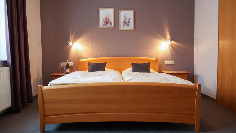 Ein gemütliches Schlafzimmer mit einem Doppelbett und zwei gemütlichen Kissen. An den Wänden hängen Bilder, und es gibt sanftes Licht von den Wandleuchten.